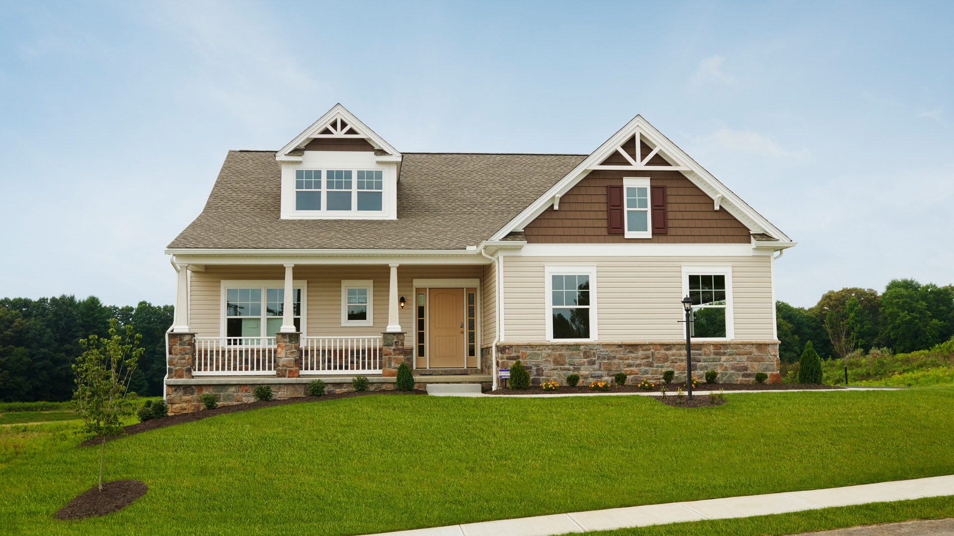 Beige ranch home exterior with stone accents, covered front porch, dormer windows, side-entry garage, and landscaped yard
