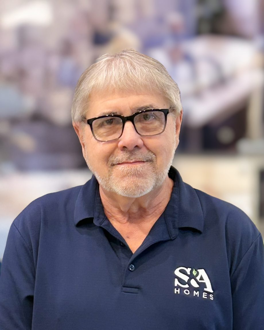 Ken Grove smiling indoors in a navy S&A Homes polo shirt and glasses