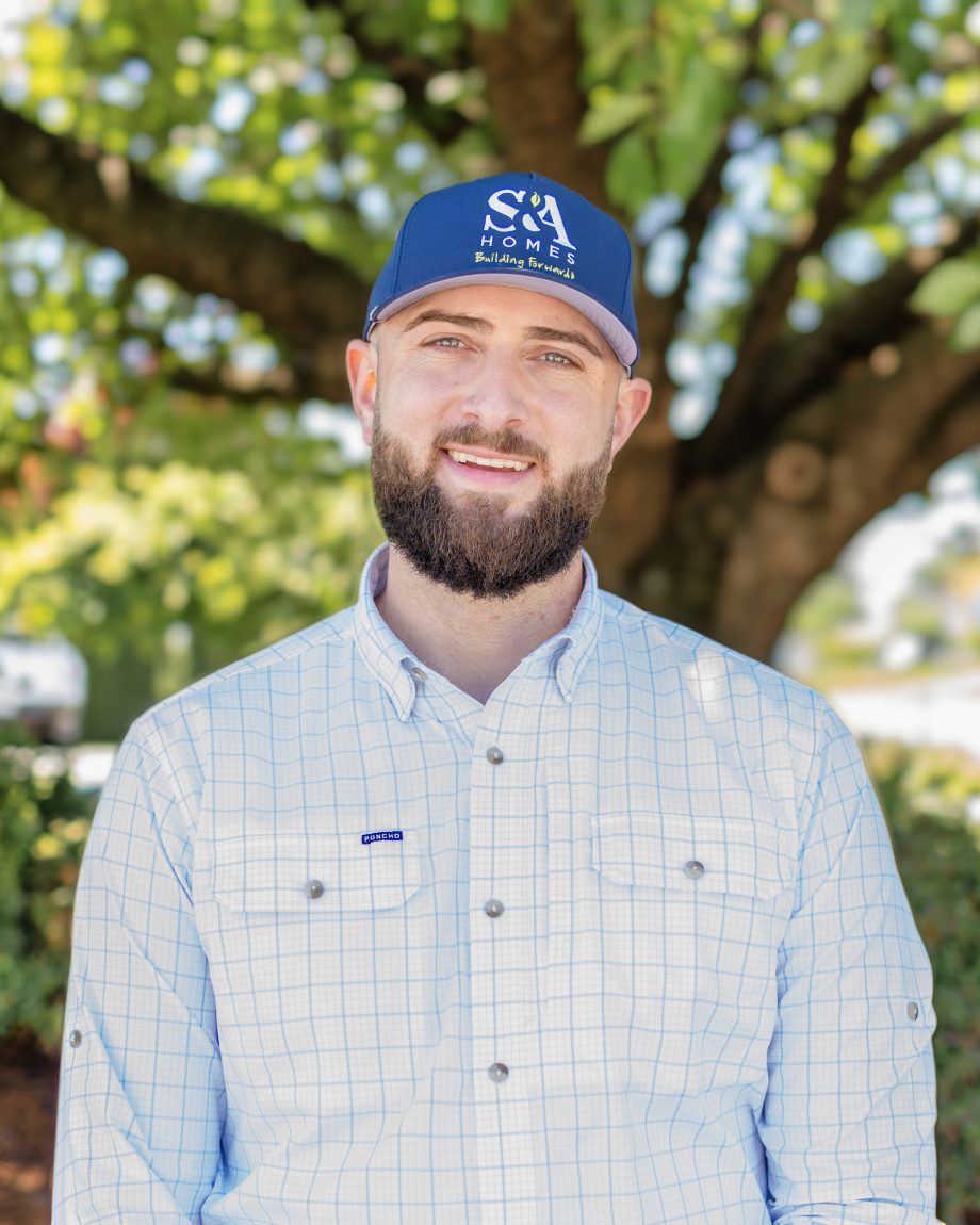 Ethan Jednat standing outdoors in a light blue button-down shirt and S&A Homes cap